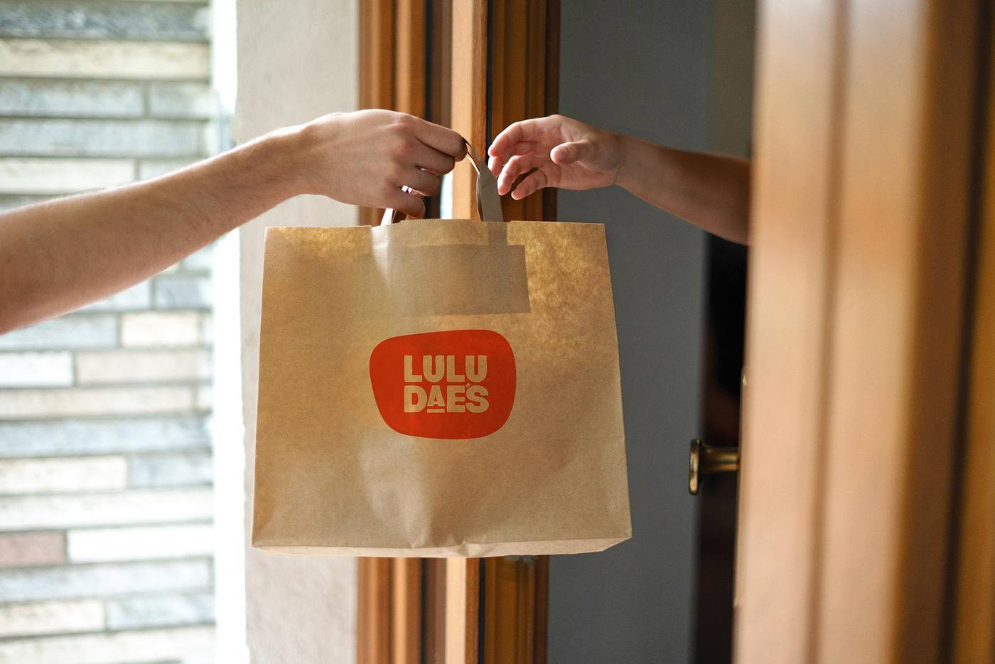 A Lulu Dae's takeaway bag being handed across a doorway